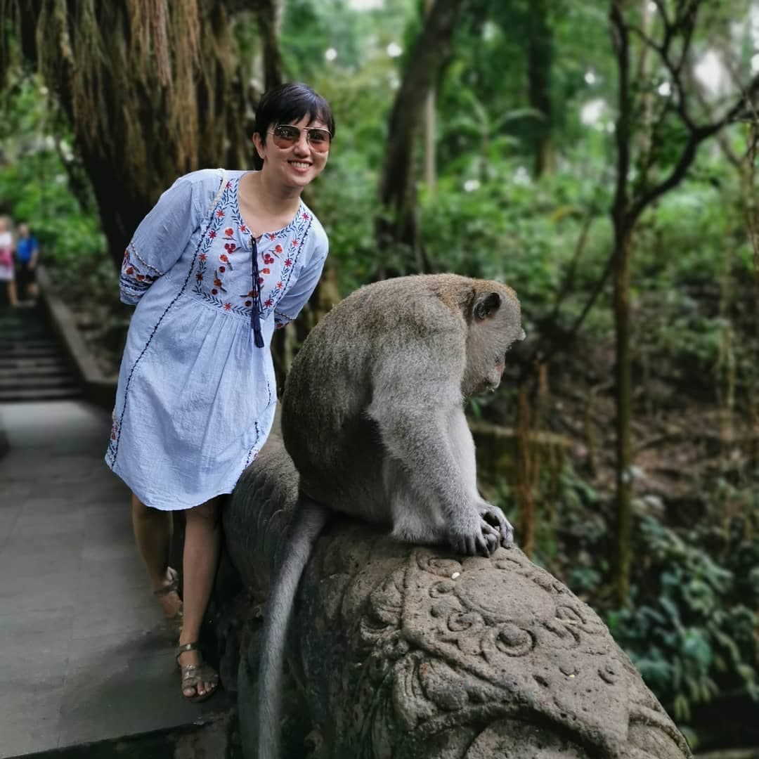 Ria Flores at the Sacred Monkey Forest Sanctuary in Ubud, Bali, posing with a long-tailed macaque on a stone sculpture