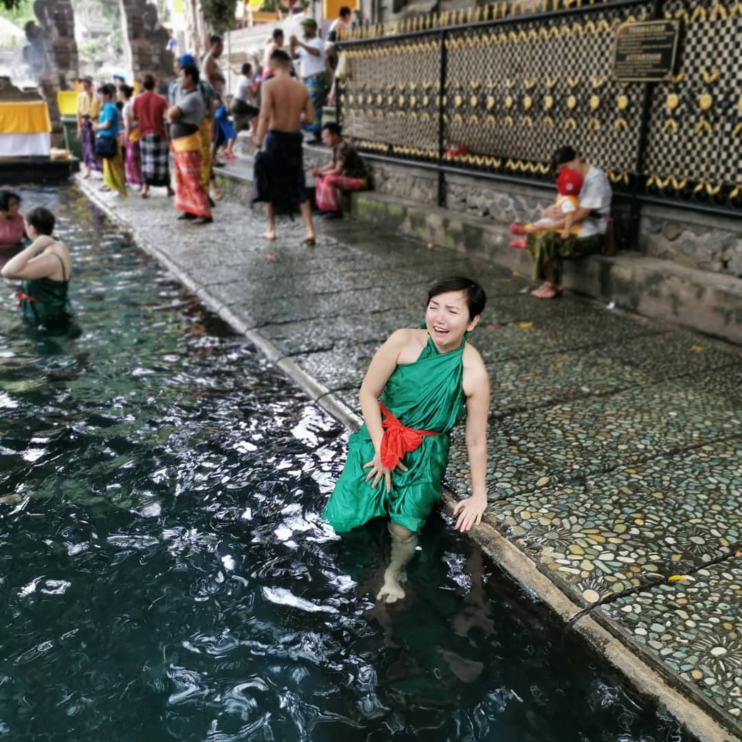 Ria Flores at Pura Tirta Empul holy spring temple in Tampaksiring, Bali, wearing a ceremonial green wrap in the purification pool