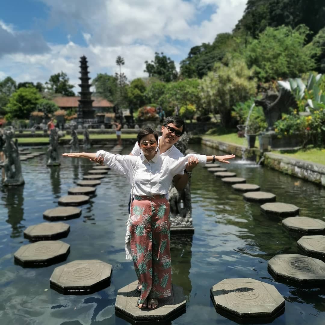Ria and Ryan Flores at Tirta Gangga Water Palace in East Bali, standing on the iconic stepping stones over the ornamental pools with the multi-tiered pagoda in the background